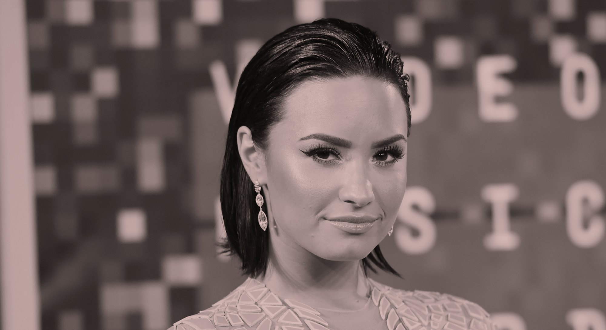 Demi Lovato, with short brown hair tucked behind ears, is wearing a pink dress