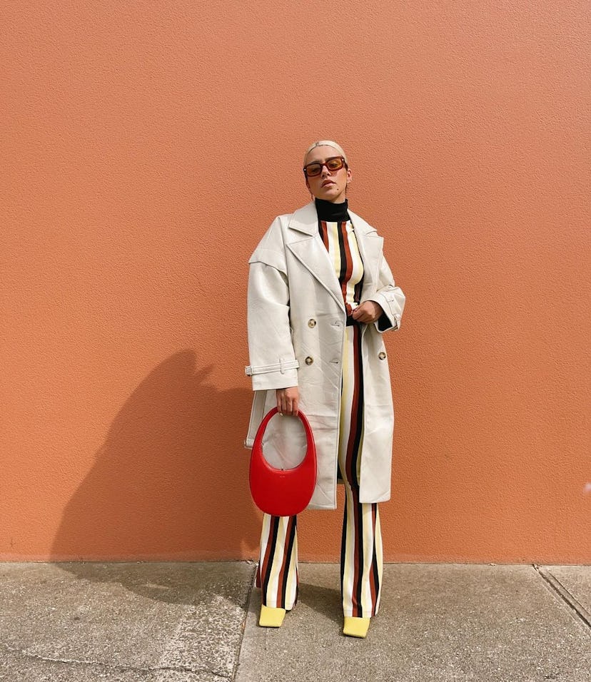 Woman wearing striped co-ord set with trench coat and red bag.