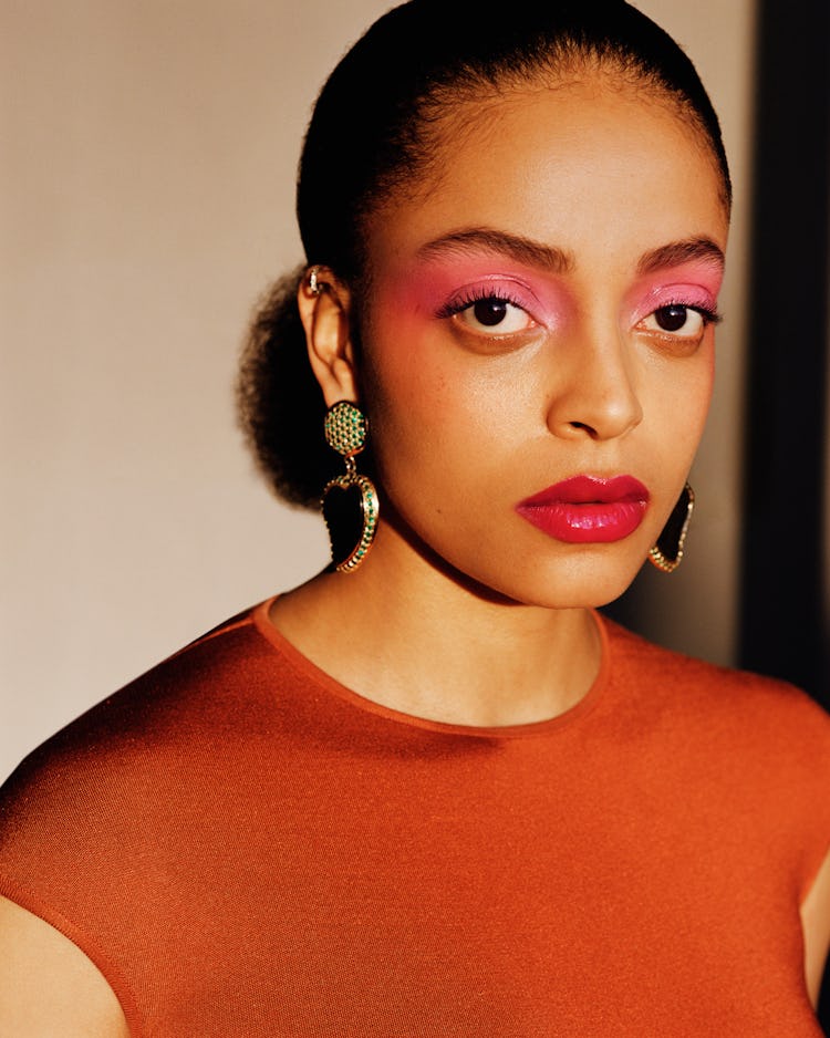 Aboah in an orange bodysuit, black earrings and pink eyeshadow 