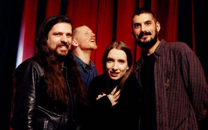 A photo of Dry Cleaning with vocalist Florence Shaw in the center. They are grinning and laughing in...