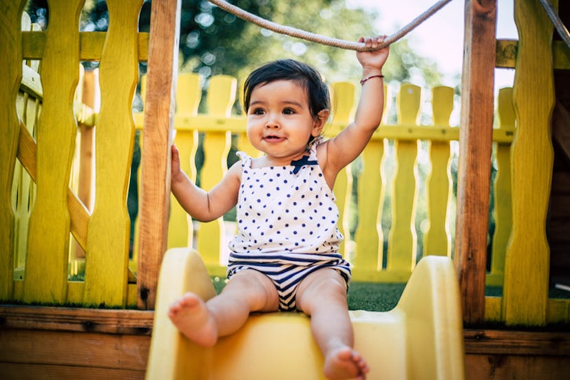 toddler sitting at top of slide at the park