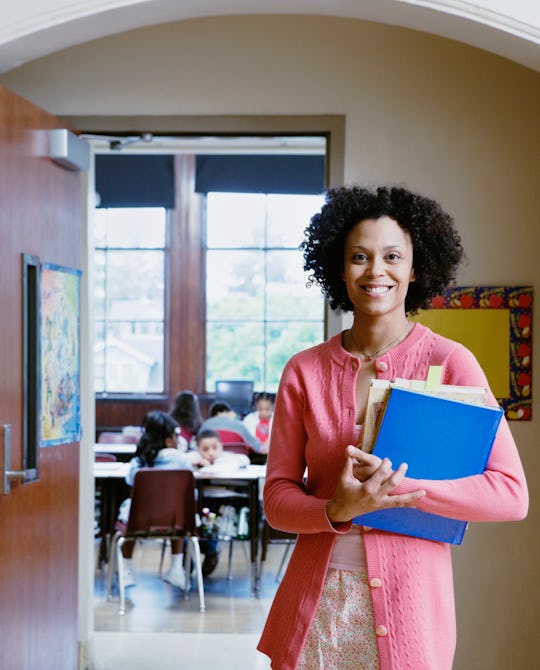 teacher standing outside of her classroom, holding a stack of folders