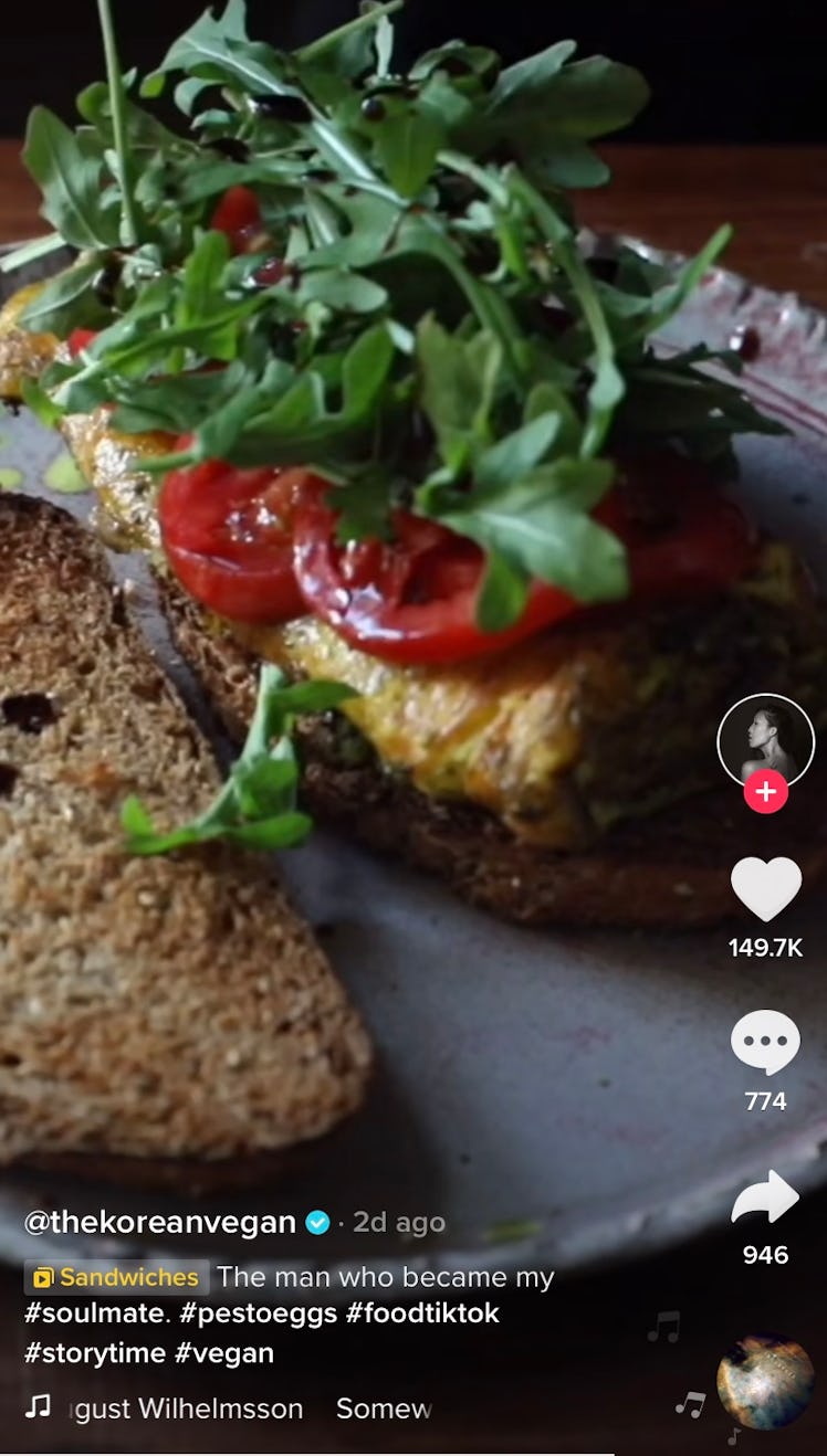 A pesto egg sandwich sits on a plate with tomatoes and arugula. 
