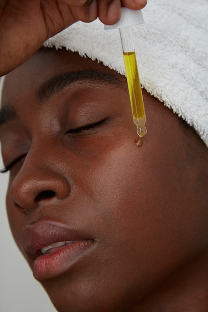 A woman with her hair in a white towel and closed eyes, applying over-the-counter retinoids with a d...