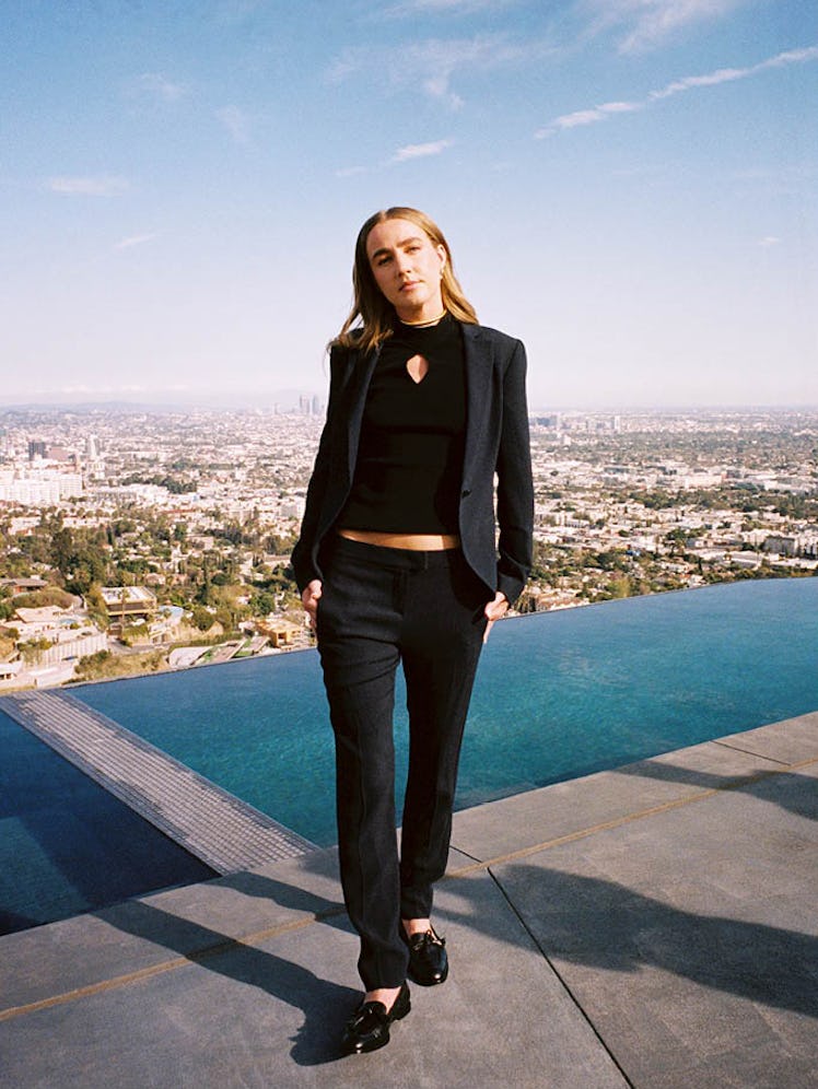 Ingrid Andress posing next to an infinity pool in a black blazer, pants, top and shoes 