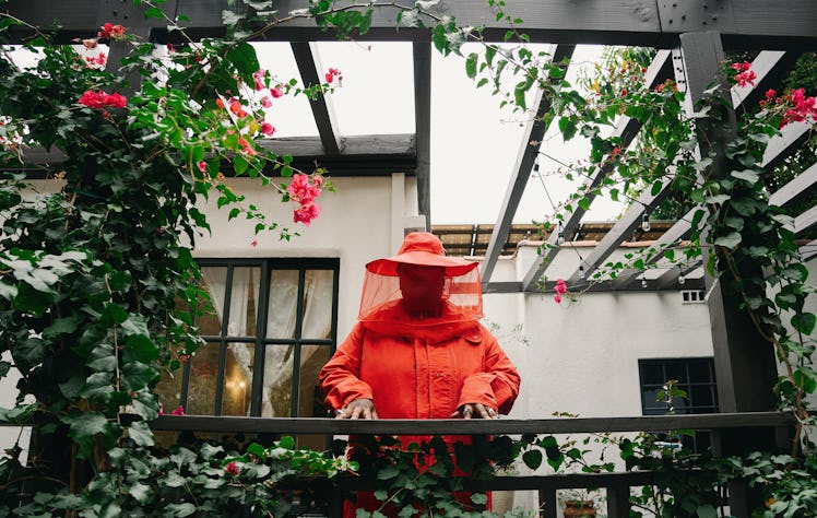 Chika standing on a balcony in an orange coat and hat 