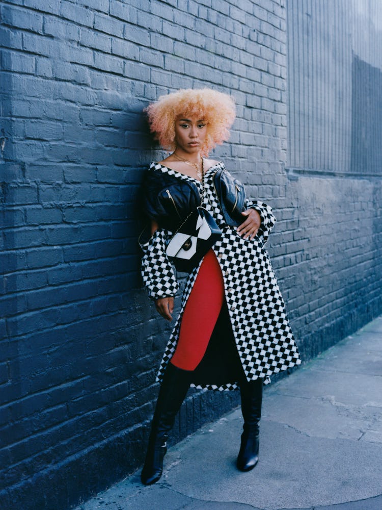 Fousheé in a Chanel checkered coat, skirt, black boots, and bag with red tights 