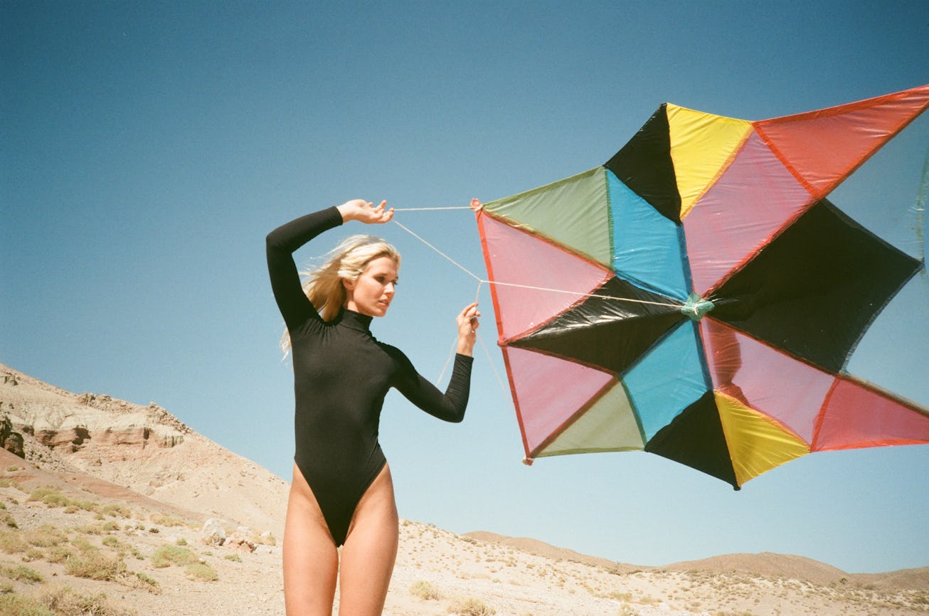 A portrait of Natalie Bergman. She wears a black leotard and is holding a colorful kite. The sky and...