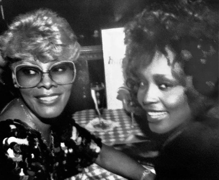 Whitney Houston and Dionne Warwick looking behind them and smiling at dinner 