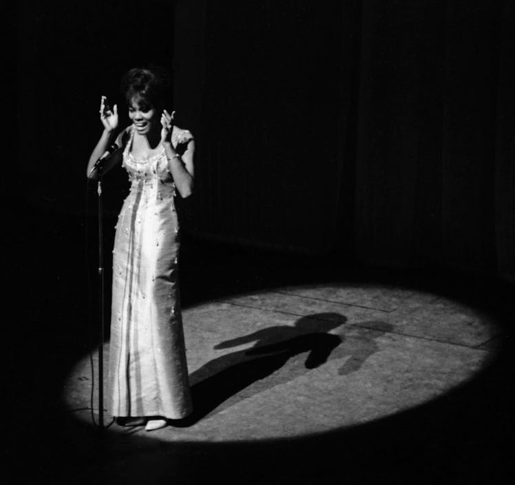 Dionne Warwick singing on stage with the spotlight on her, in a long bedazzled dress