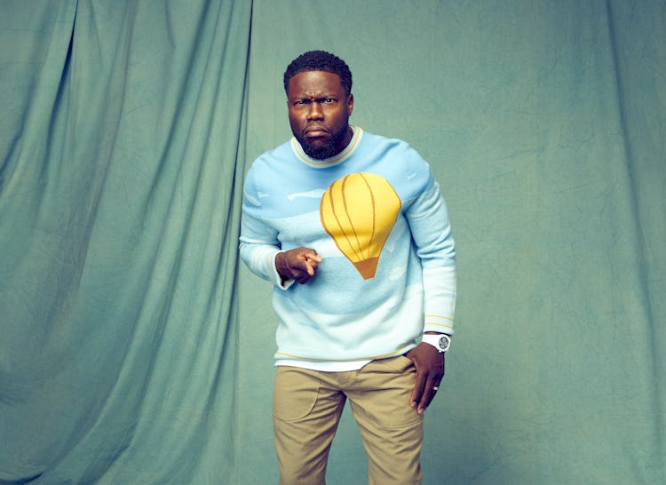 Kevin Hart points at the camera while wearing a blue Victor Li sweater with a yellow hot air balloon...