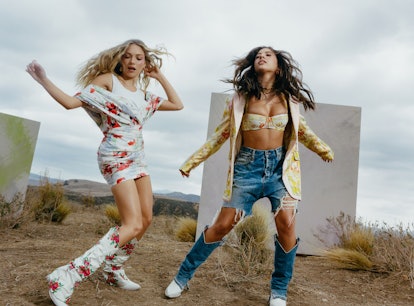 Two BFFs posing; a woman in a white floral dress an boors and a woman in a yellow blazer, bralette a...