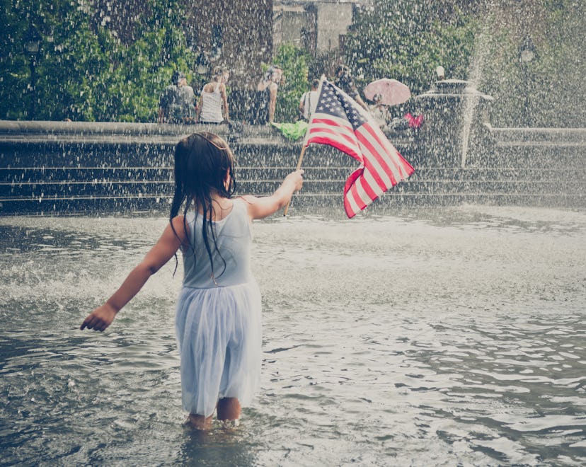 A young girl playing in a park fountain, holding the American Flag