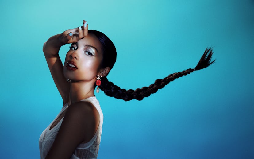 Olivia rodrigo in a white tank top, with her hand leaning on her forehead, turquoise nail polish and...