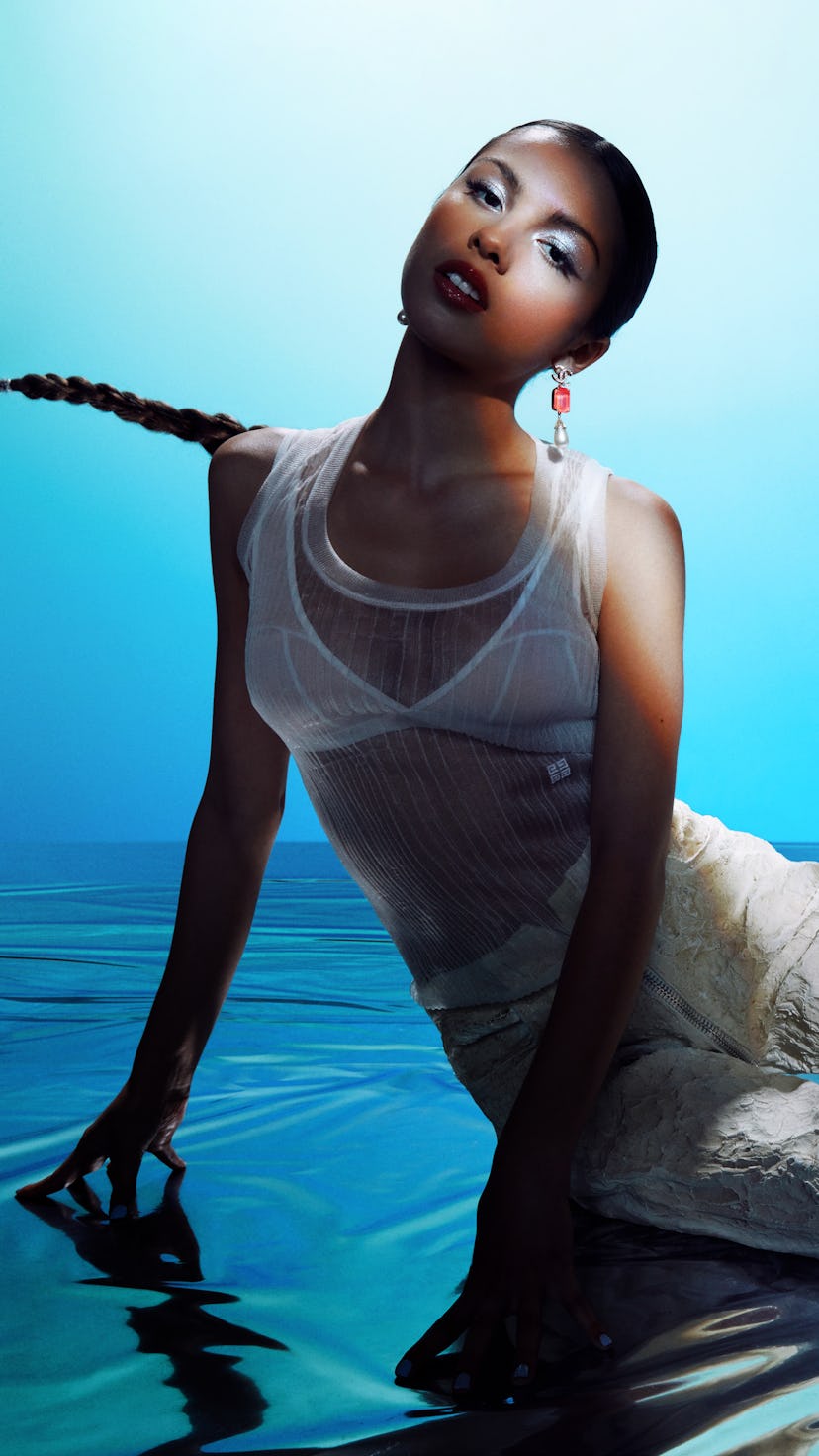Olivia Rodrigo in a white see through combination on a watery surface.