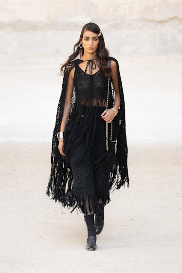 A model walking while wearing a sheer black Chanel cape and dress