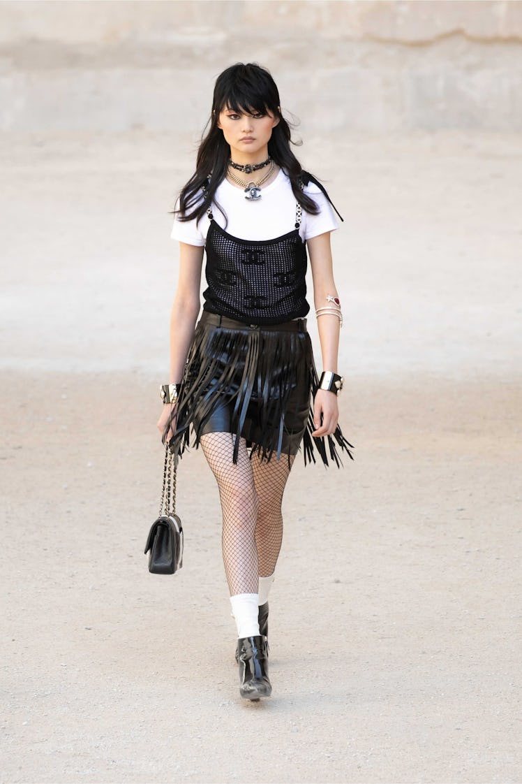 A model walking while wearing a Chanel fringe skirt, white tee, and a black tank top
