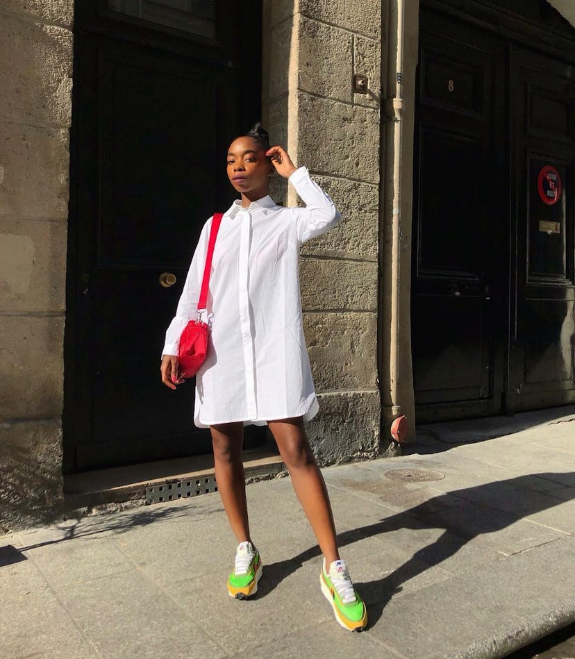 Aude Julie wears a classic white button-down dress, neon sneakers, and a red bag.