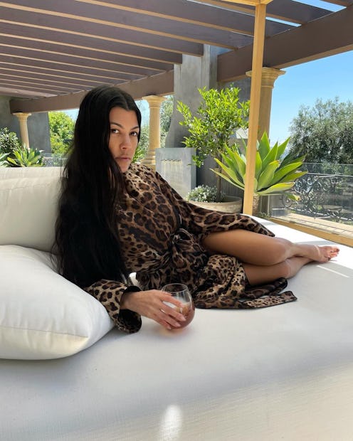 kourtney kardashian lounging on a white chair with a glass of collagen juice