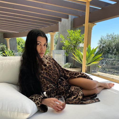 kourtney kardashian lounging on a white chair with a glass of collagen juice