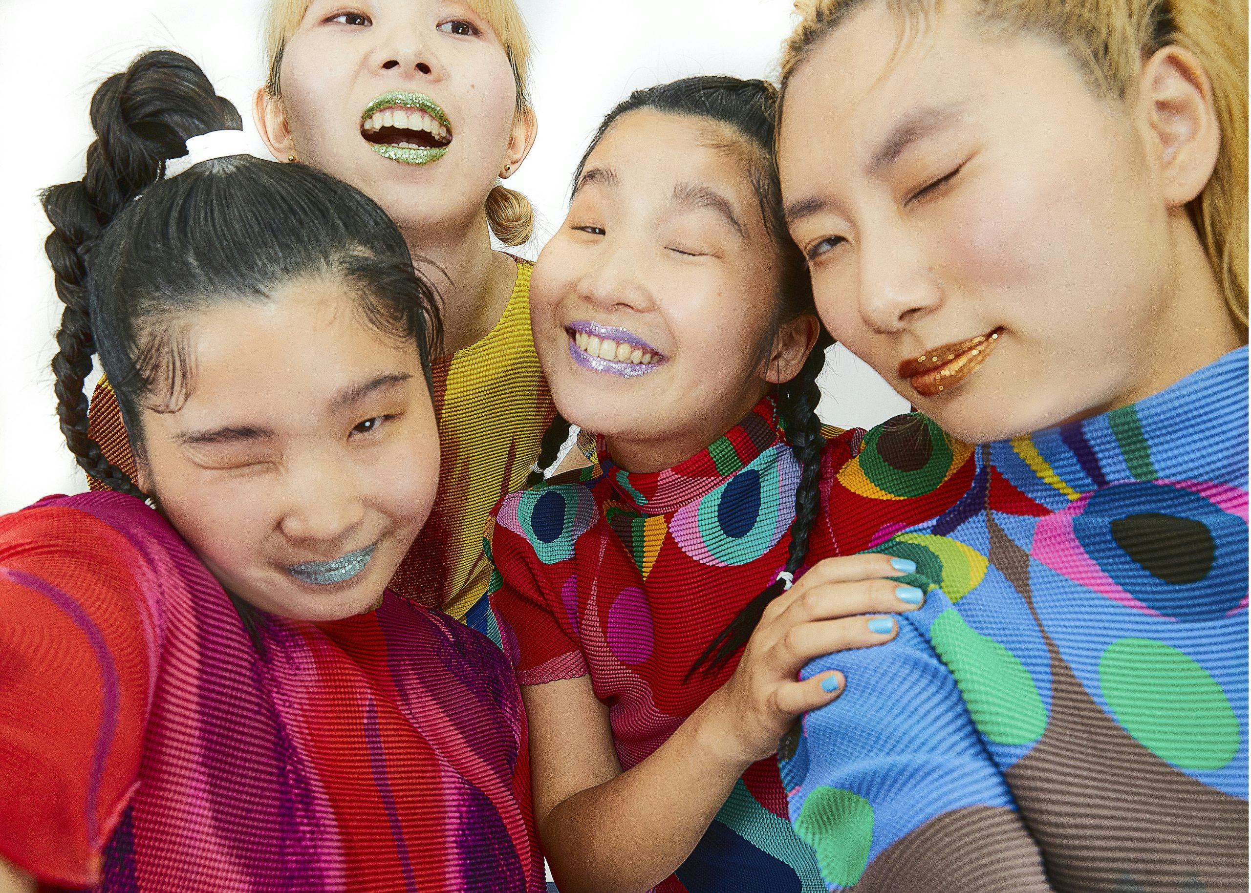 A photo of CHAI. The four members are wearing colorful tops, and all winking into the camera. They a...