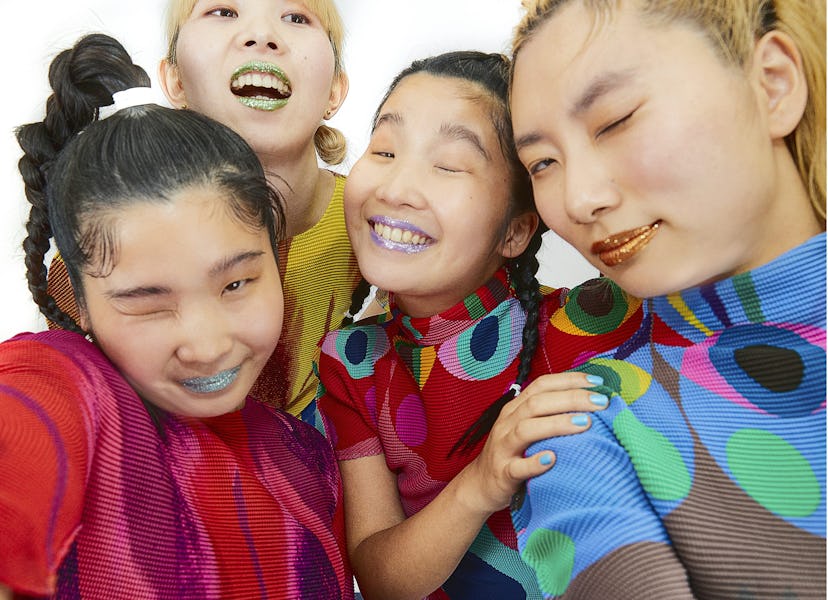A photo of CHAI. The four members are wearing colorful tops, and all winking into the camera. They a...