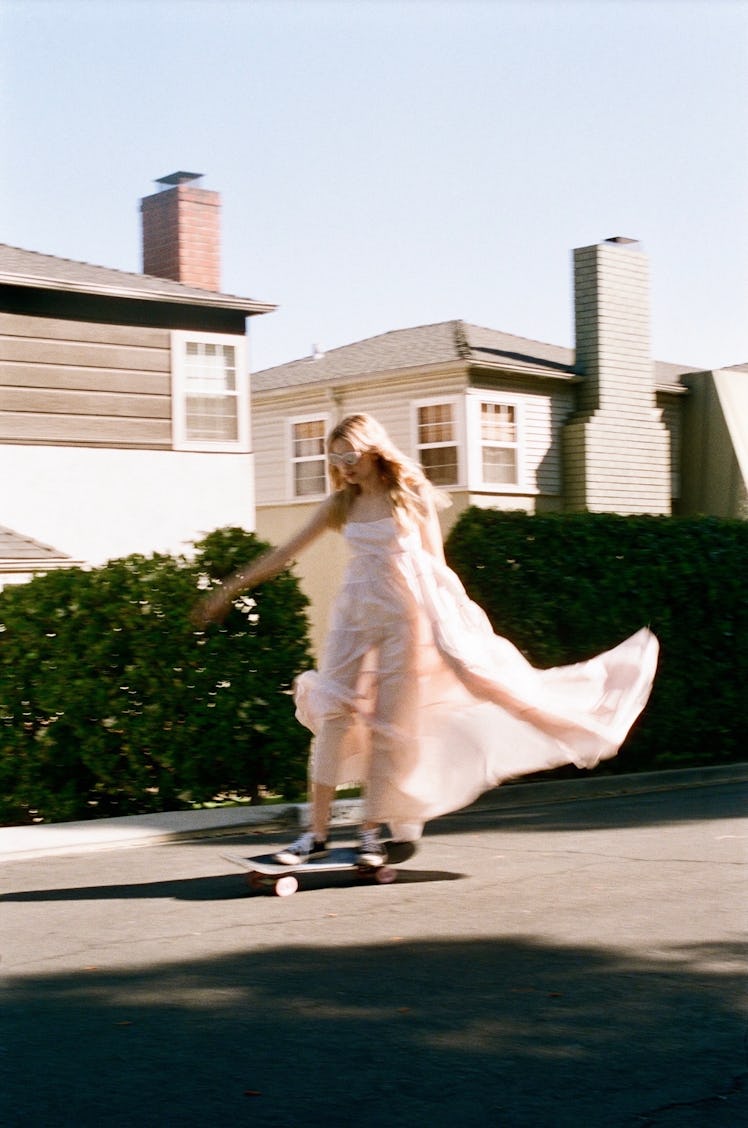 Olivia Scott Welch riding a skateboard in a beige gown and black converse 