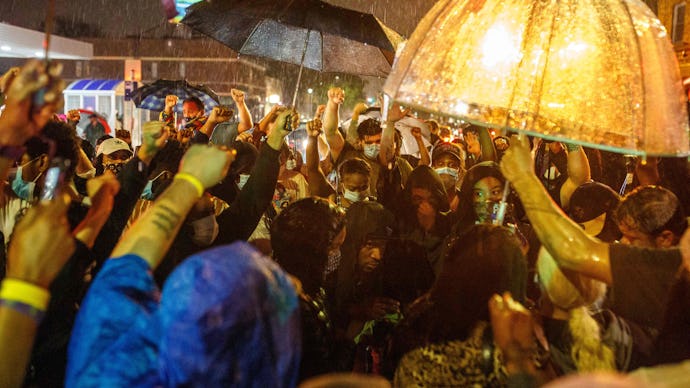 Protesters gathering in the rain in Minneapolis with umbrellas and rain coats