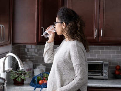 pregnant woman drinking water by kitchen sink
