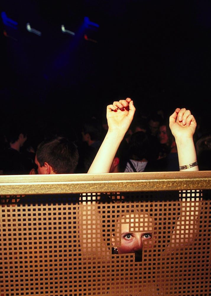 A woman with her arms raised looking through a partition in a club