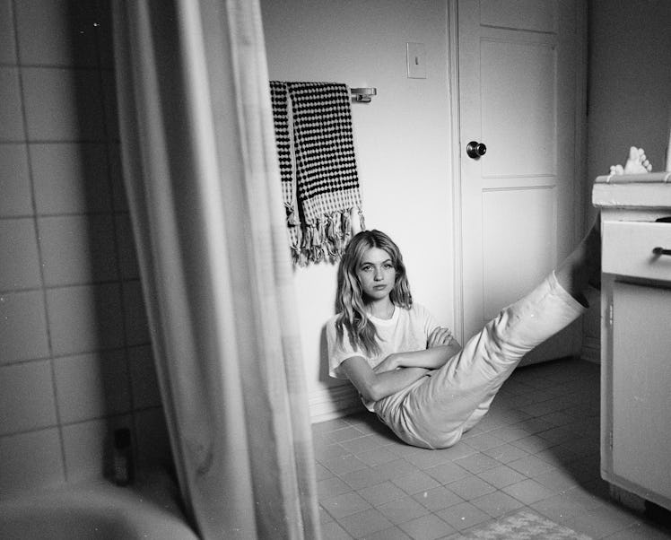 Black and white photo of Olivia Scott Welch sitting on the bathroom floor with her legs up on a coun...