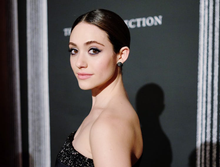 Emmy Rossum with her hair slicked back in a blue off-the-shoulder dress looking over her shoulder at...