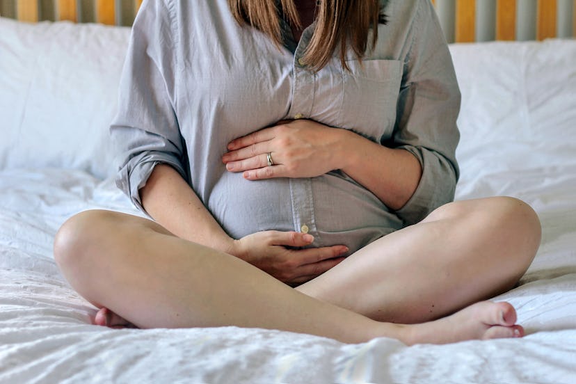 pregnant woman sitting cross-legged on bed, holding her stomach 