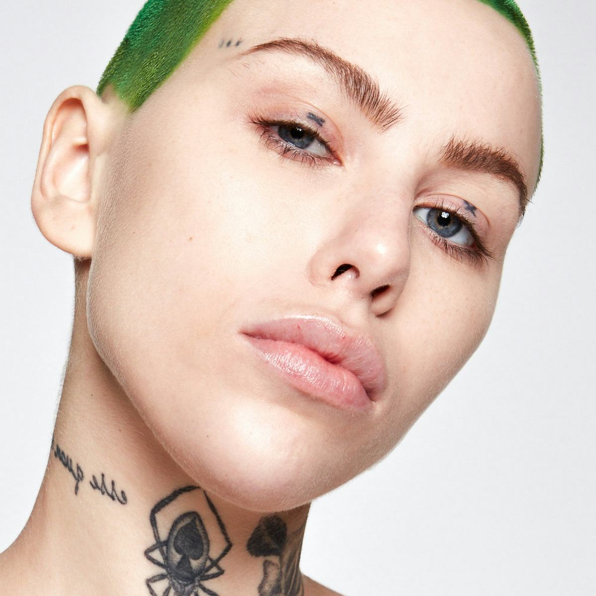 A model with tattoos and green hair modeling Kosas Tinted Face Oil, one of several skin tints that are best for lightweight coverage.