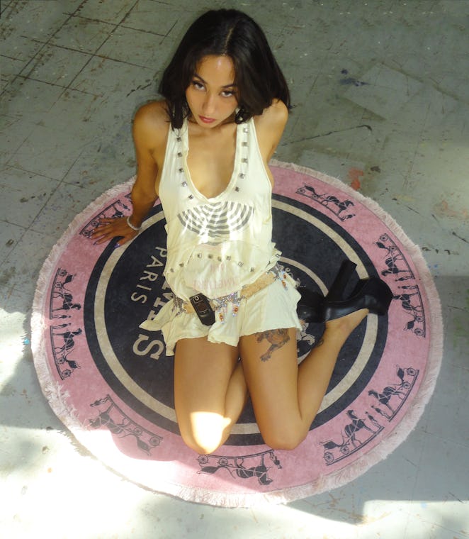 Singer Isabella Lovestory sitting on the floor in a white Undercover Spring 2006 shirt, black thrift...