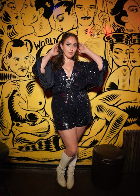 Catherine Coheh posing in a black sequin dress in front of a black-yellow painted wall