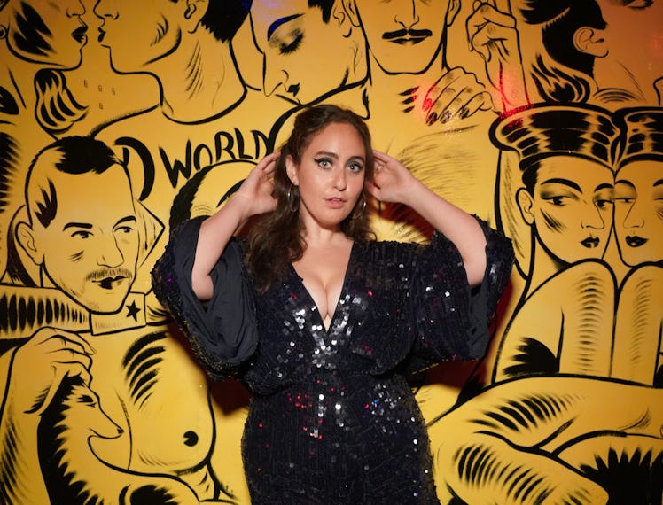 Catherine Coheh posing in a black sequin dress in front of a black-yellow painted wall