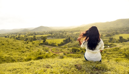 Woman sitting on a hill and staring out into a field.