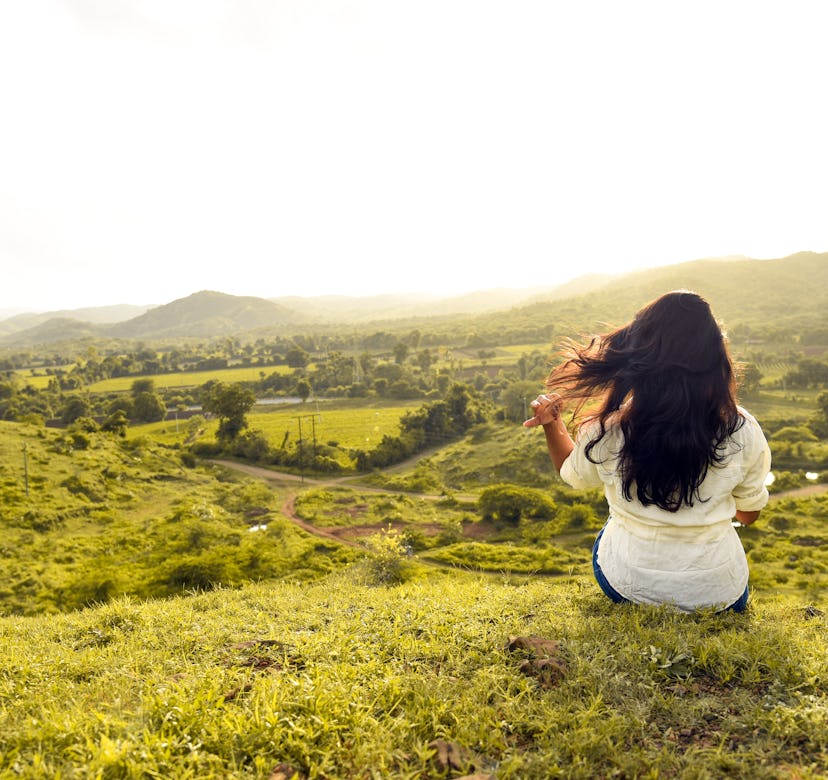 Woman sitting on a hill and staring out into a field.