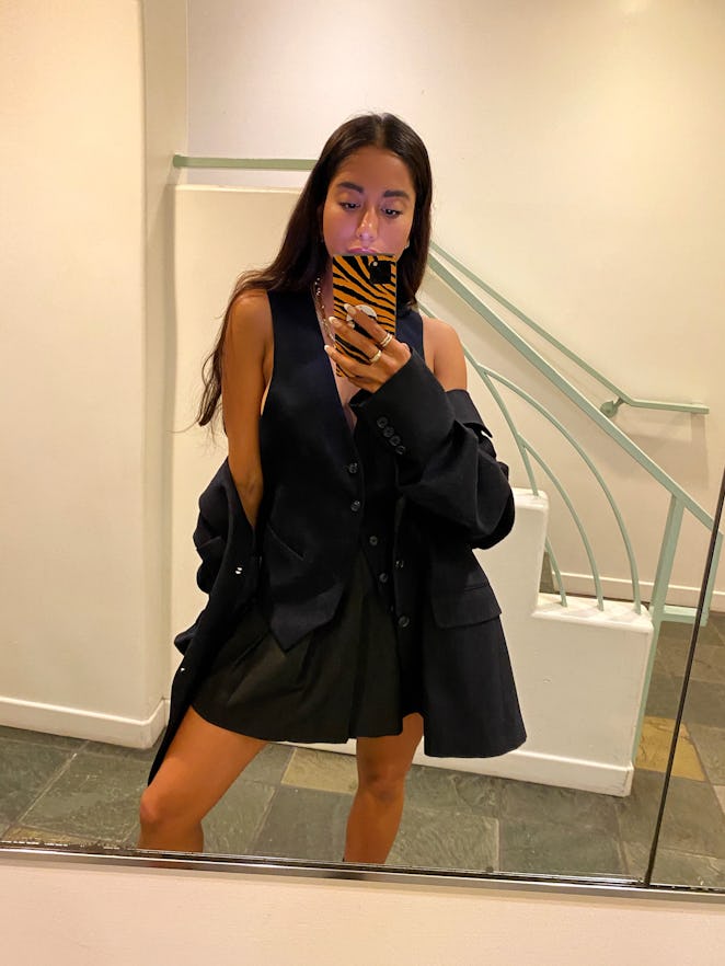 DJ Amrit taking a photo of herself in the mirror while wearing a thrifted black vest and thrifted bl...