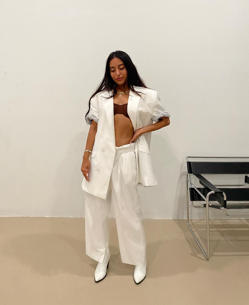 DJ Amrit posing in a white Daily Paper suit with a brown bra underneath and white high-heeled boots 