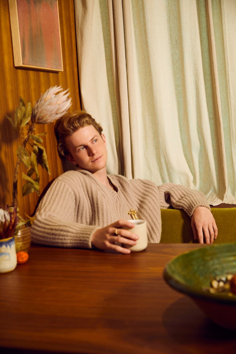 Gem chef Flynn McGarry wears a tan Prada sweater and sits at a table holding a coffee mug.