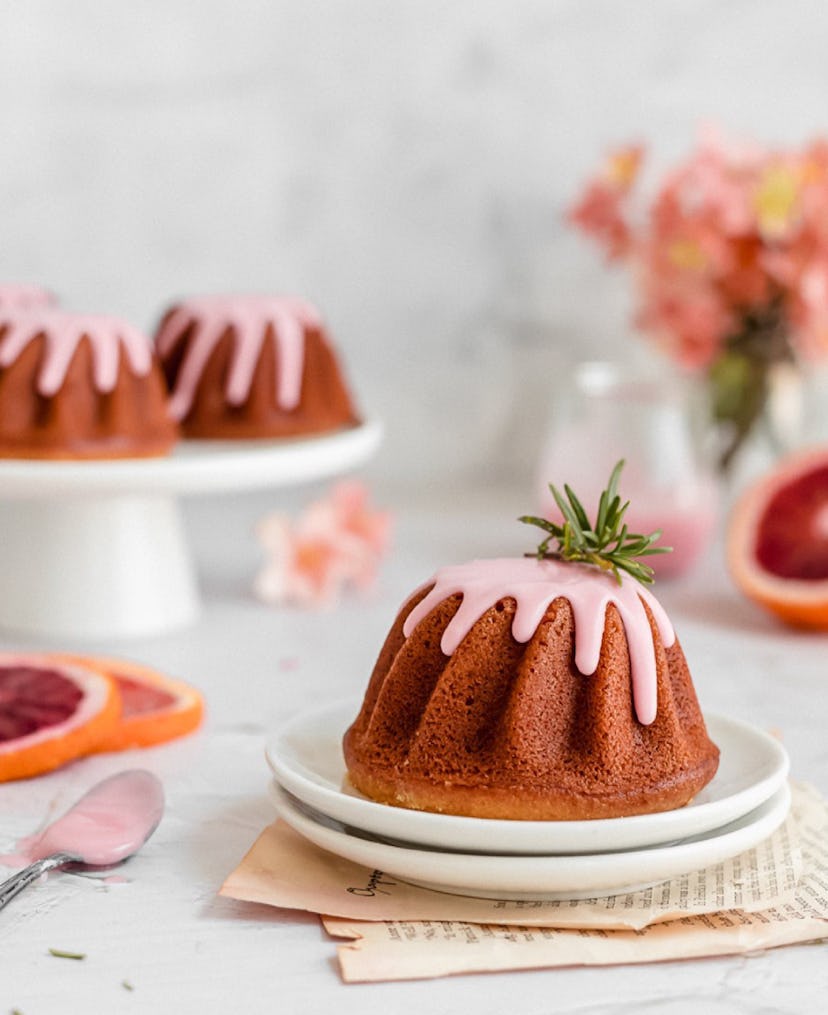 Plate with a blood orange bundt cake topped with pink icing; tray of bundt cakes out of focus behind...