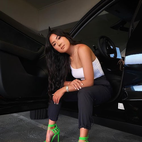 Janette Ok poses in white tanktop, black pants, and green heels.