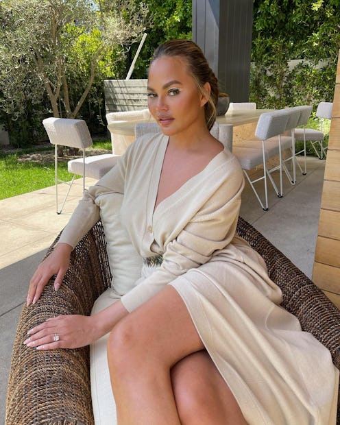 chrissy teigen sitting in a lounge chair wearing white graphic eyeliner