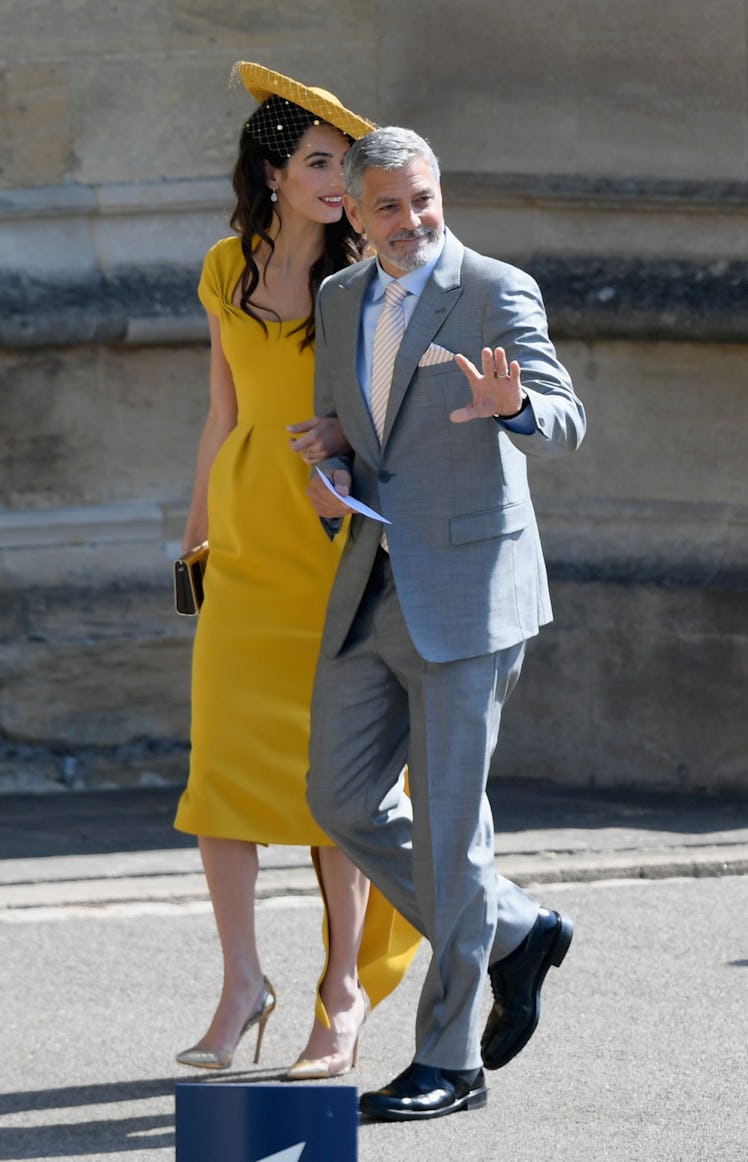 Amal Clooney in a yellow gown and hat, George Clooney in a gray suit