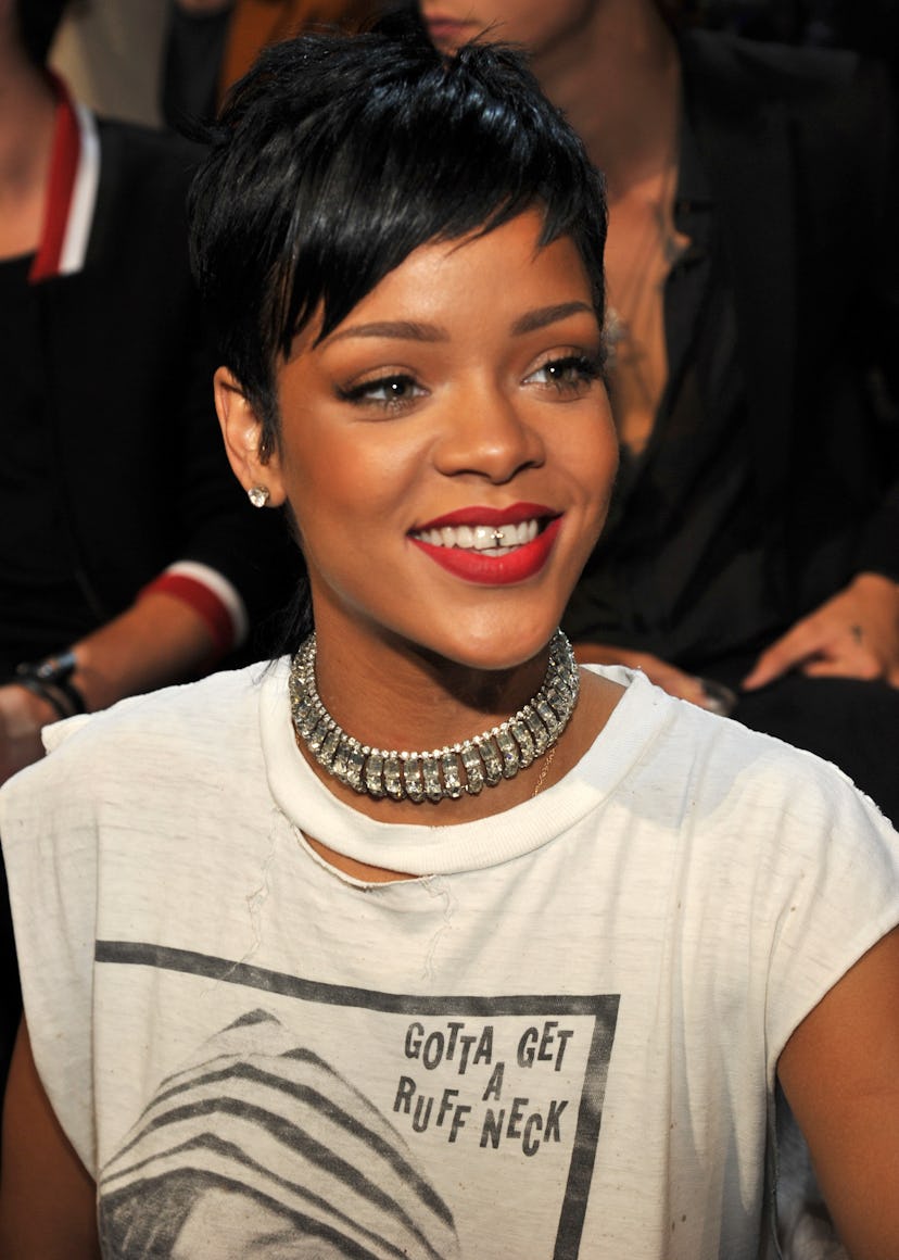 Rihanna smiling, wearing her iconic dark-haired Pixie cut and red lipstick