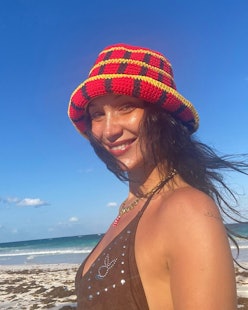 a photo of bella hadid smiling on the beach with a red hat on and dark hair