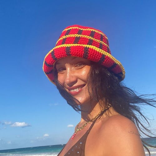a photo of bella hadid smiling on the beach with a red hat on and dark hair