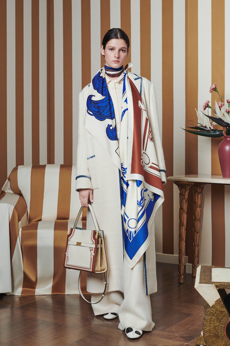 Model posing while wearing a white Tory Burch coat and baggy pants combination with a blue, white, a...